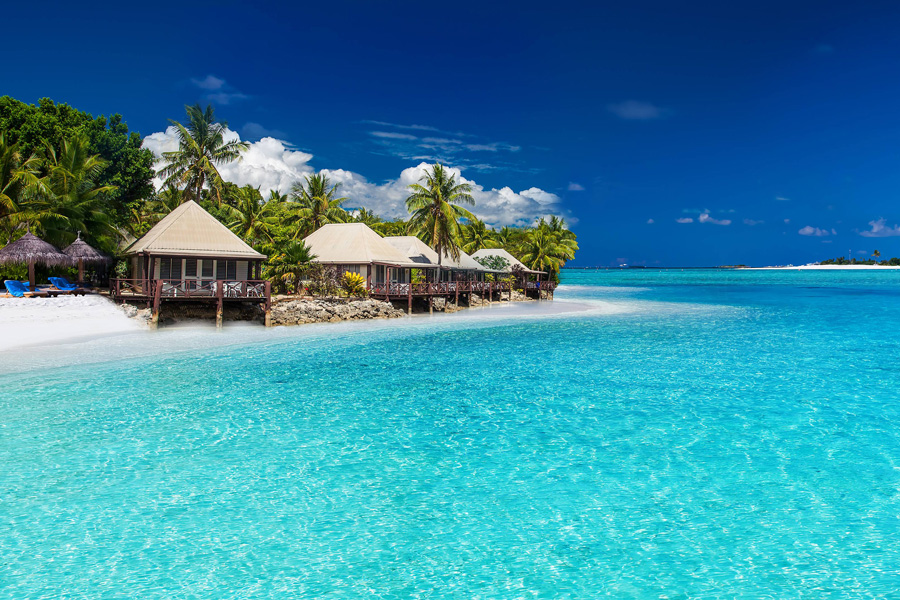 Turkosblått hav, palmklädd strand och karaktäristiska beach huts på Fiji.