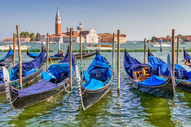 Blå gondoler ligger förtöjda i vattnet utanför Venedig.